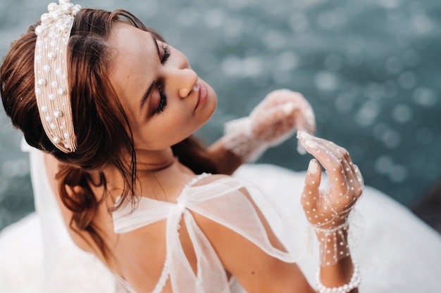 Una novia elegante con un vestido blanco, guantes y los pies descalzos está sentada cerca de una cascada en el parque disfrutando de la naturaleza.Una modelo con un vestido de novia y guantes en un parque natural.Belarús. foto en blanco y negro