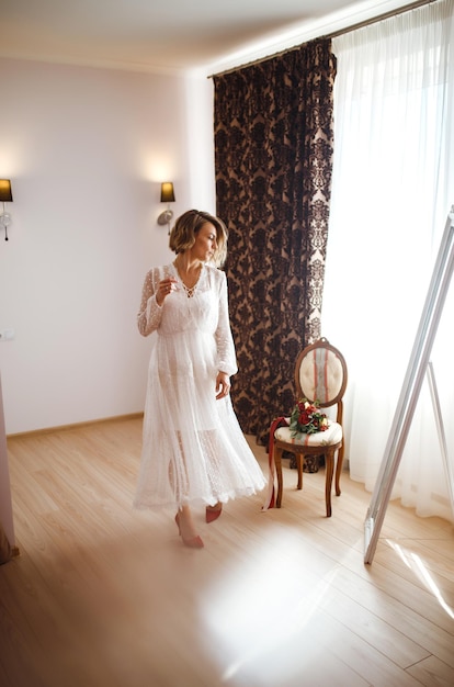 Novia con elegante vestido blanco mirándose en el espejo La novia sonríe y posa frente al espejo