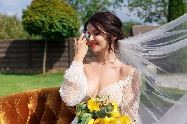 La novia encantadora guarda un ramo de novia y se sienta en el patio.