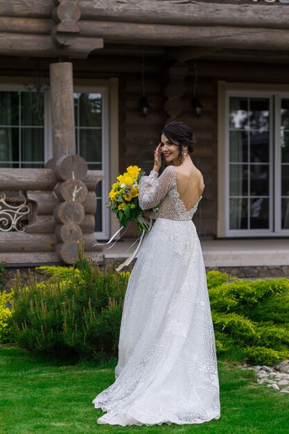 La novia encantadora mantiene un ramo de novia y posa en el patio.