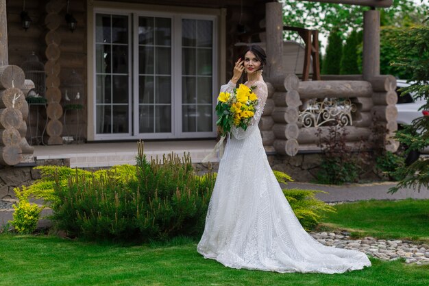 La novia encantadora mantiene un ramo de novia y posa en el patio.