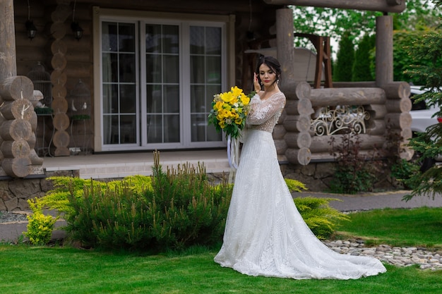 La novia encantadora mantiene un ramo de novia y posa en el patio.