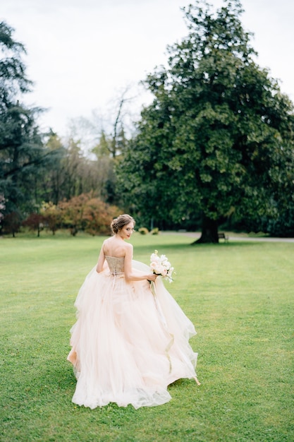 La novia se encuentra de espaldas a la cabeza con un vestido rosa con un ramo de flores.