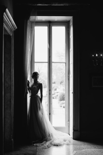 La novia está de pie junto a una gran ventana girando hacia los lados del lago de como