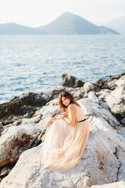 Novia con estilo se sienta en un vestido pastel de novia en un acantilado sobre el mar