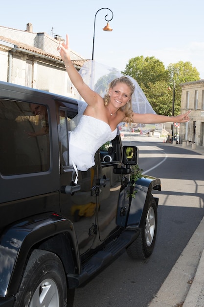 La novia feliz en el auto de la boda se divierte junto a las ventanas