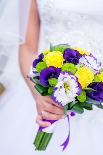 La novia feliz tiene un ramo de novia en las manos. Ramo de novia de flores púrpuras, amarillas y blancas en sus manos y una joven novia.