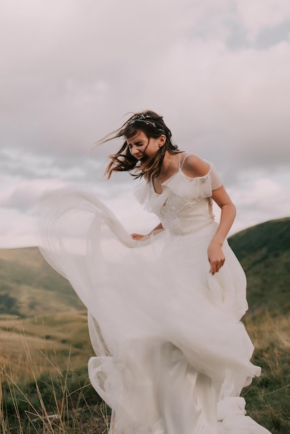 Novia feliz en vestido de novia blanco sonriendo contra el telón de fondo de las montañas