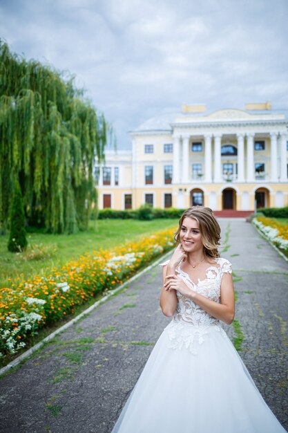 Novia hermosa chica con un vestido blanco con un tren caminando en el fondo de una casa grande con columnas en el día de su boda