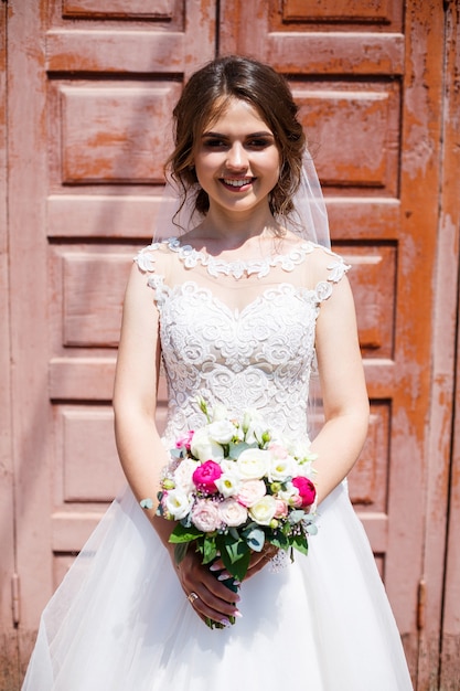 Novia hermosa chica con un vestido blanco y un velo posando hermosamente y sonriendo en el día de la boda