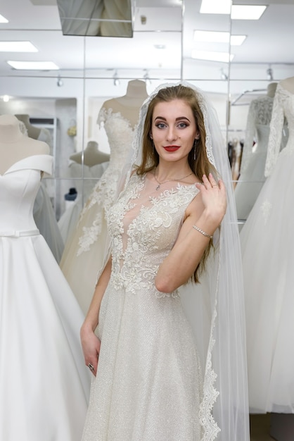 Novia hermosa joven eligiendo vestido y velo en el salón