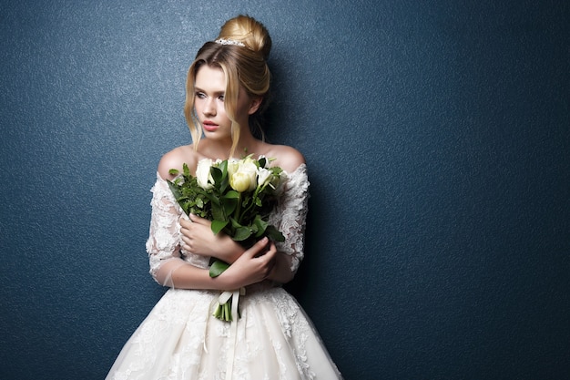 Novia hermosa joven. Peinado de novia, cabello rubio, vestido de novia, maquillaje y ramo de novia. Tiro de interior