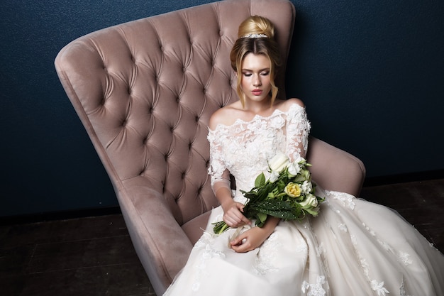 Novia hermosa joven. Peinado de novia, cabello rubio, vestido de novia, maquillaje y ramo de novia. Tiro de interior