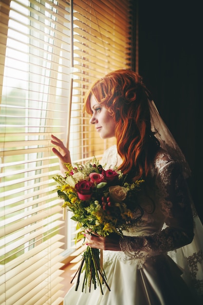 Novia hermosa del pelo rojo cerca de la ventana