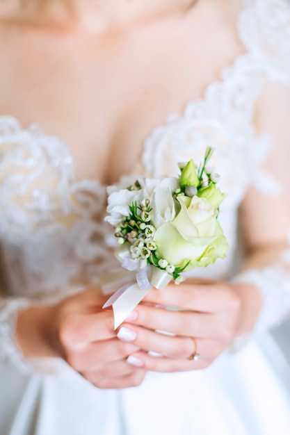 La novia con un hermoso vestido blanco sostiene un ramo para el novio que se fijará en su chaqueta