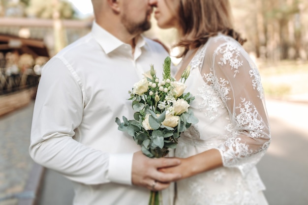 Una novia con un hermoso vestido con una cola sosteniendo un ramo de flores y vegetación.