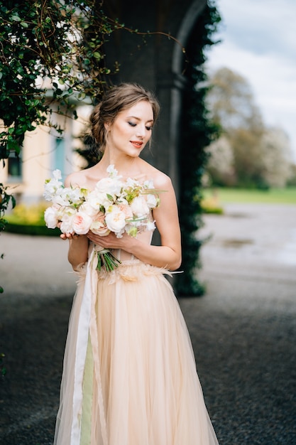 La novia con un hermoso vestido con hombros descubiertos tiene un ramo de flores rosas