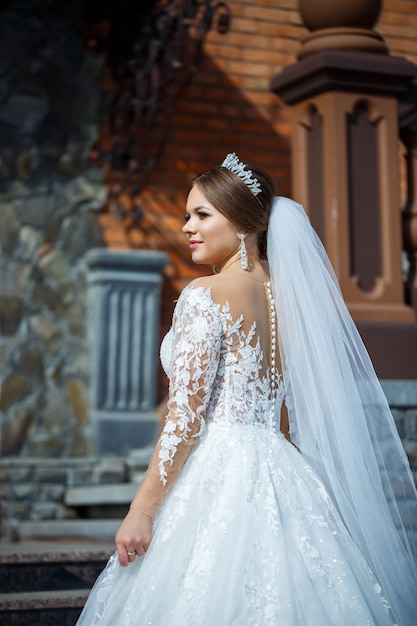 Novia en un hermoso vestido largo y blanco sobre un fondo de un edificio de ladrillo