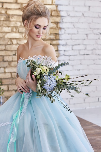 Novia con un hermoso vestido turquesa en previsión de la boda. Rubia en vestido de encaje verde mar con ramo. Novia feliz, emoción, alegría en su rostro. Hermosos maquillajes, manicuras y peinados de mujeres.