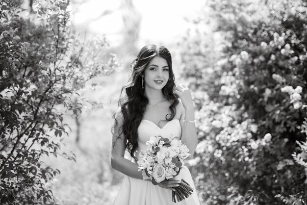 Novia joven con un vestido blanco en un bosque de primavera en arbustos de lilas