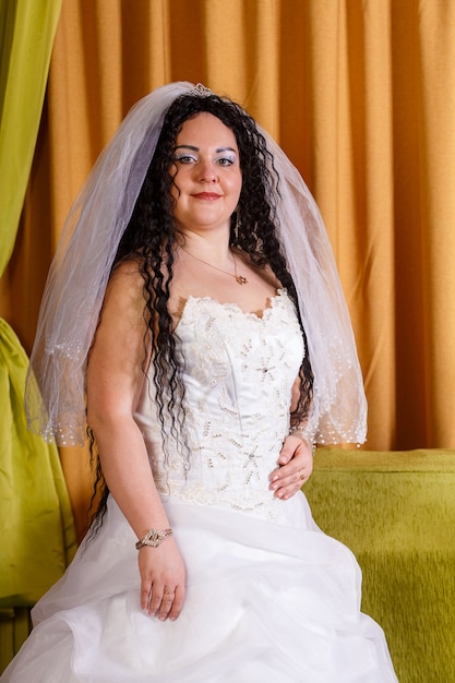 Una novia judía con un vestido blanco con velo se encuentra en la habitación esperando al novio para la ceremonia de la jupá.