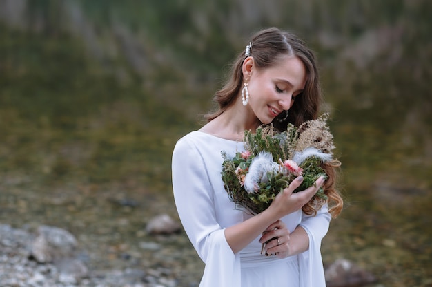 Una novia en un largo vestido de novia de pie en la orilla de un lago