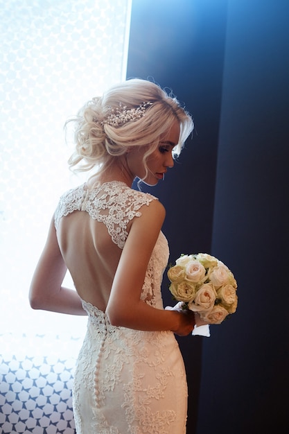 Novia de la mañana Una mujer en un vestido de novia blanco con un ramo de flores en sus manos. Hermosa chica rubia preparándose para la ceremonia de boda