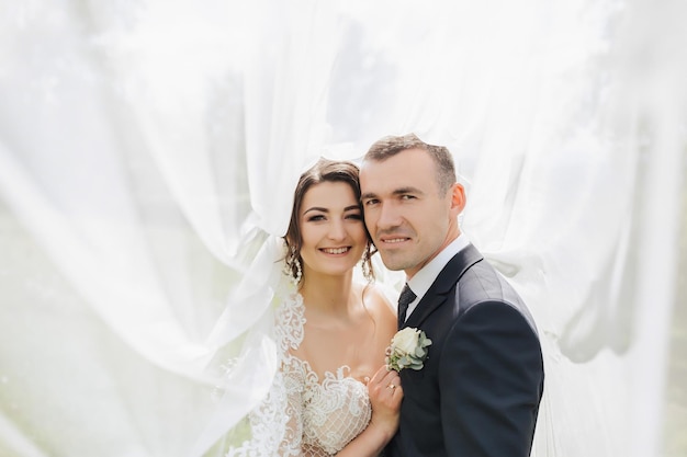 Una novia morena de cabello rizado en un vestido blanco y un novio velado abrazan y besan Retrato de la novia y el novio Hermoso maquillaje y cabello Boda en la naturaleza