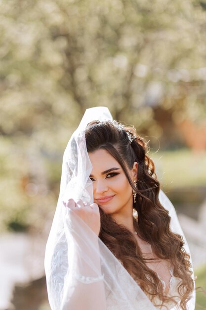 Foto novia morena rizada posa envuelta en un velo contra el fondo de montañas y casas de madera vestido magnífico con mangas largas busto abierto boda de verano