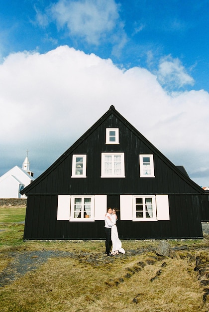 La novia y el novio se abrazan cerca de la casa de madera negra Islandia