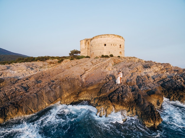 La novia y el novio se abrazan en la costa rocosa cerca de la antigua fortaleza arza