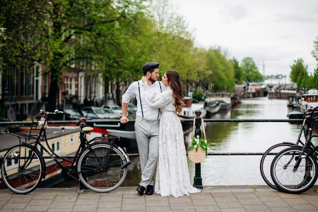 La novia y el novio se abrazan en el puente junto a la bicicleta. Boda retro estilizada.