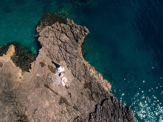 La novia y el novio se acuestan uno al lado del otro en la orilla rocosa y miran vista superior