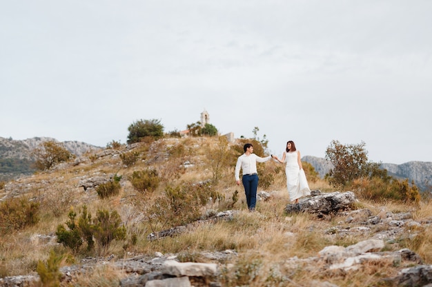 La novia y el novio bajan por la ladera de la montaña el novio sostiene la mano de las novias