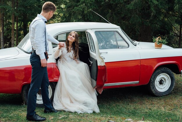 Novia y novio en el bosque cerca del coche de bodas de lujo