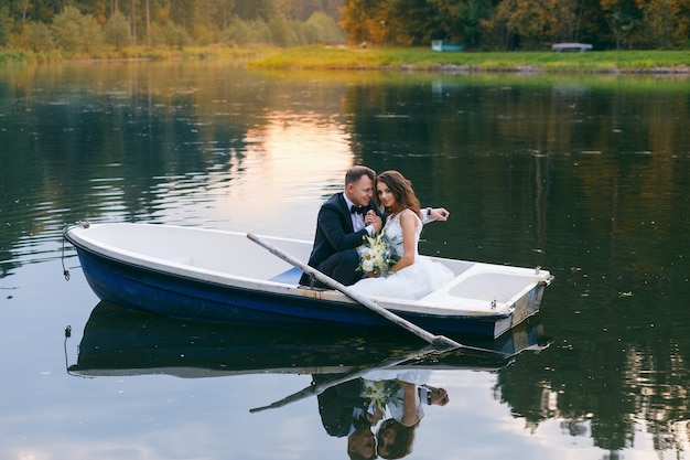 La novia y el novio en un bote de remos en el lago al atardecer