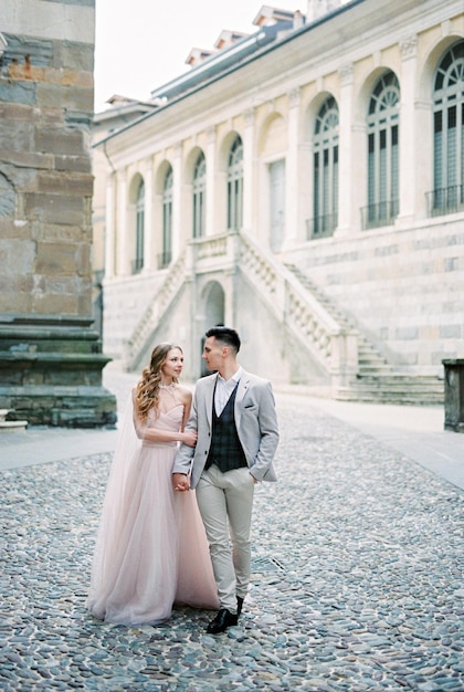 La novia y el novio caminan cogidos de la mano cerca del antiguo edificio Bérgamo Italia