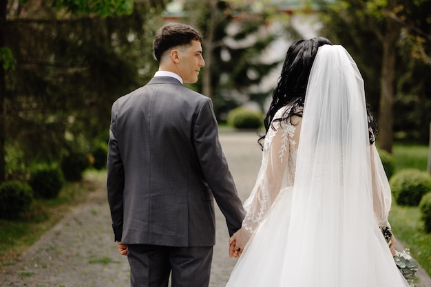 Una novia y un novio caminan de la mano, tomados de la mano, tomados de la mano, y el vestido del novio lleva un vestido de novia.