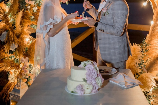 Novia y novio cerca del arco de boda con pastel