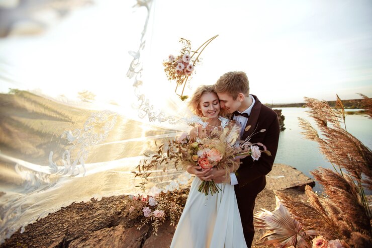 La novia y el novio cerca de la decoración de la boda en una ceremonia en un acantilado de roca cerca del agua al atardecer. Velo volando del viento