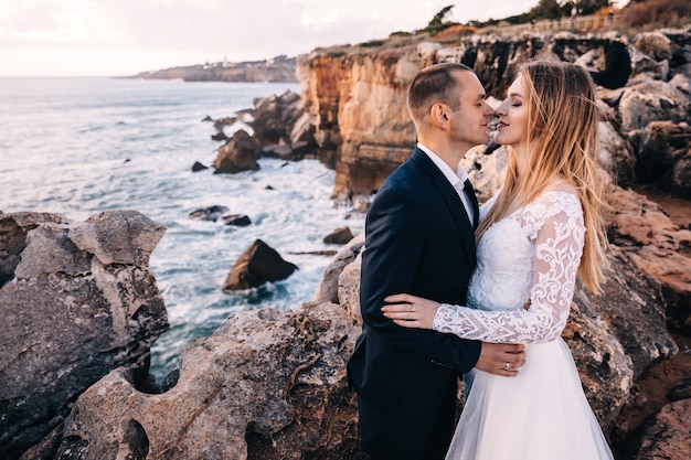 La novia y el novio cerraron los ojos y se abrazaron en el fondo de las rocas altas y el mar.