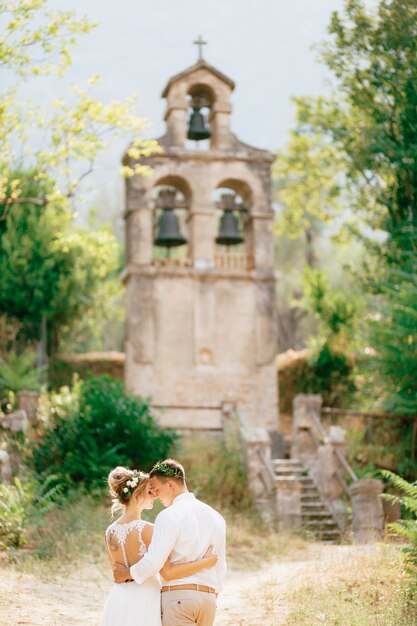 La novia y el novio en coronas abrazándose en el antiguo campanario cerca de la iglesia en prcanj