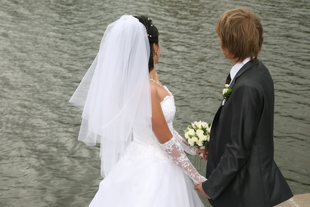 La novia y el novio se dan la mano y miran el agua.