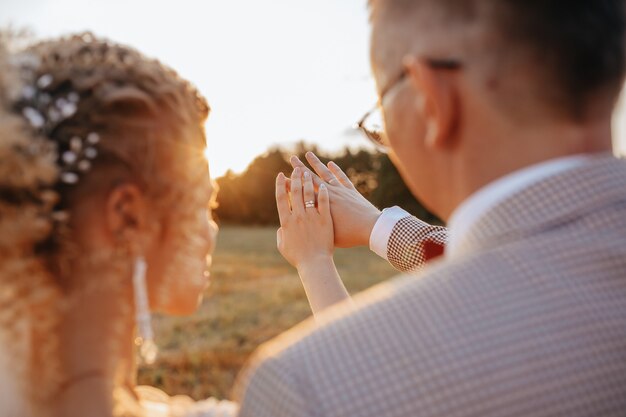 La novia y el novio en el día de la boda abrazan y miran anillos al atardecer