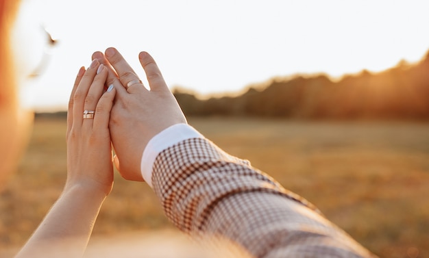 La novia y el novio en el día de la boda abrazan y miran anillos al atardecer