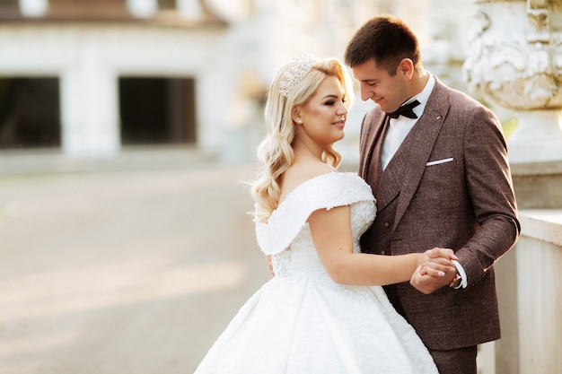 Novia y el novio en el día de la boda caminando al aire libre en la naturaleza de primavera. Novios, recién casados feliz mujer y hombre abrazando en parque verde. Amorosa pareja de boda al aire libre.