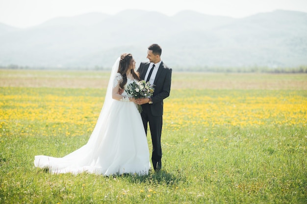 La novia y el novio en el día de la boda caminando al aire libre en la naturaleza verde de verano.