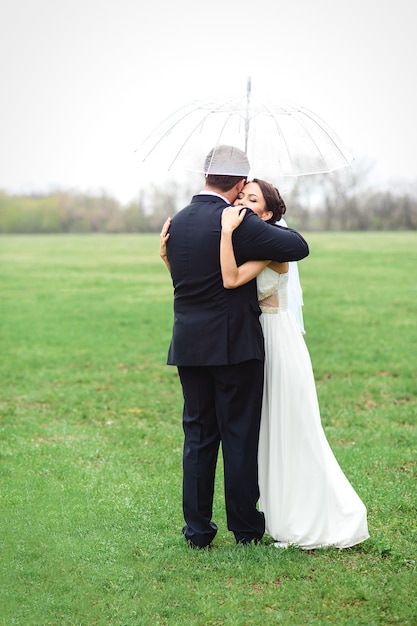 La novia y el novio en un día lluvioso de boda caminando bajo un paraguas