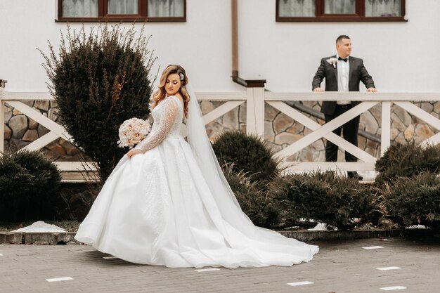 Foto la novia y el novio están caminando cerca del hotel y posando felices y disfrutando del día tomados de la mano un largo tren en el vestido boda de invierno