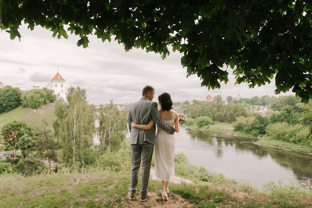 La novia y el novio están de espaldas a la orilla del río y contra el fondo del casco antiguo